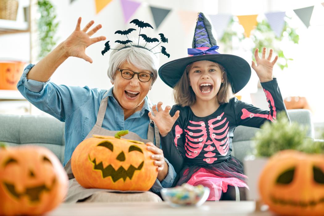 A senior woman and her granddaughter smiling together, enjoying Halloween activities.